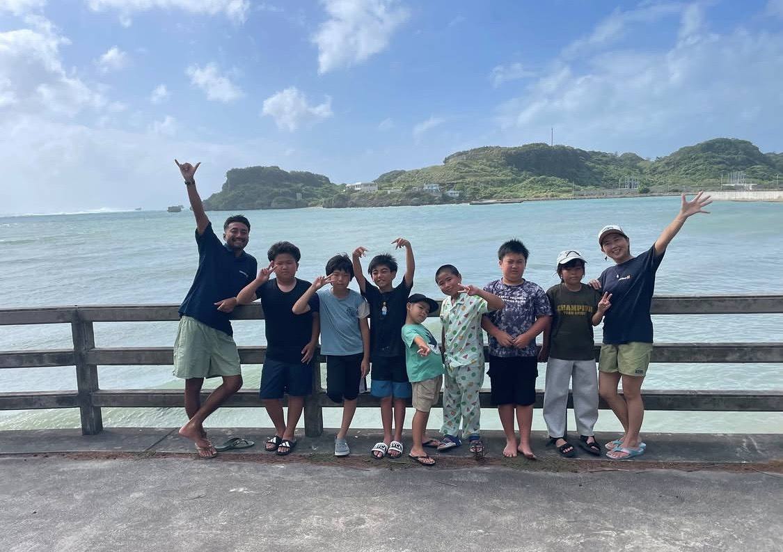 宮城島の海を背に桟橋で並ぶ子どもたち7名とスタッフ