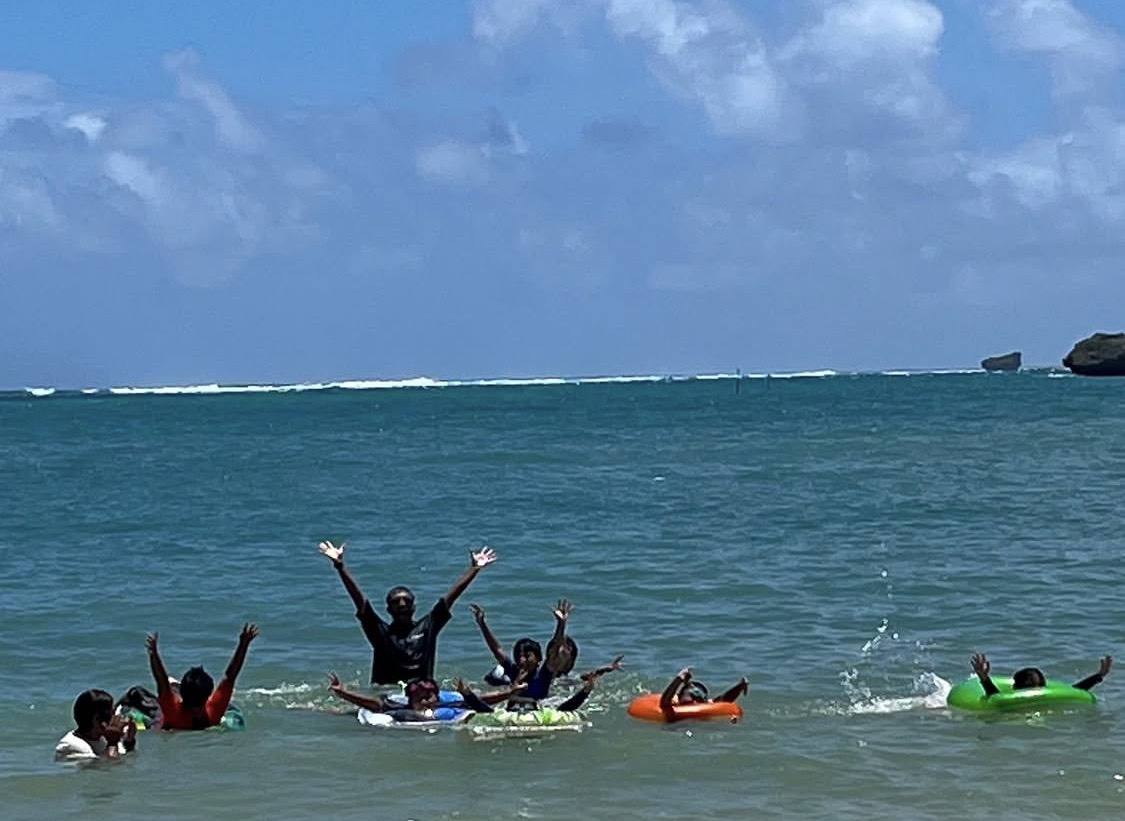 浮き輪を使って海で遊ぶ子どもたちと、両手を上げて応えるスタッフ