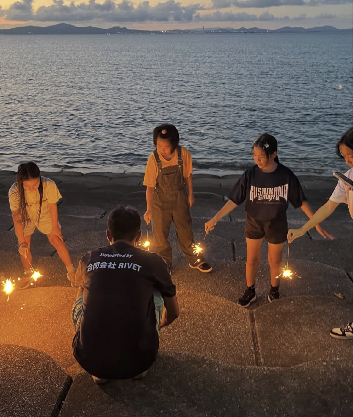 夕暮れの海辺で線香花火をする子どもたち