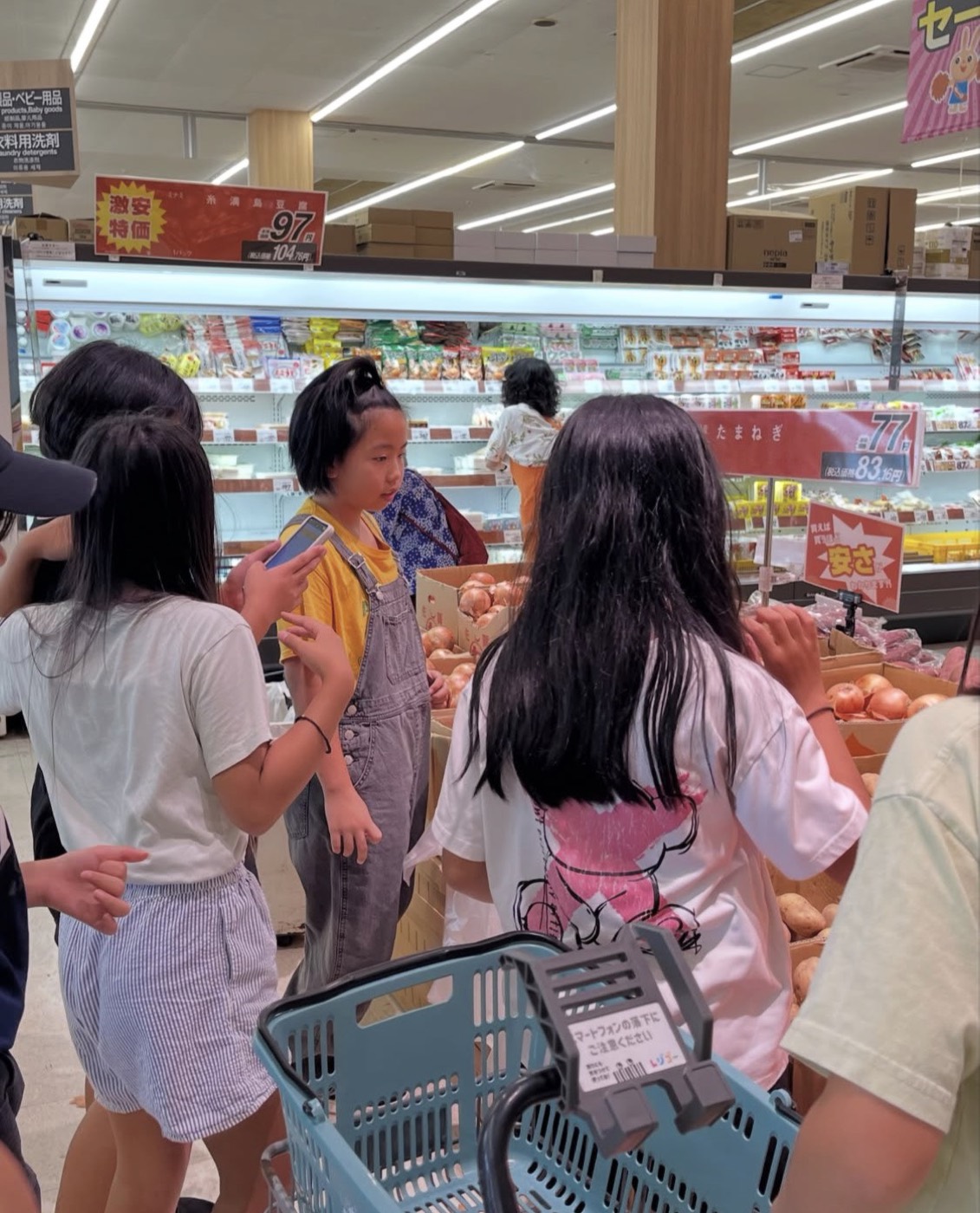 スーパーで玉ねぎやじゃがいもを選びながら買い出しをする子どもたち