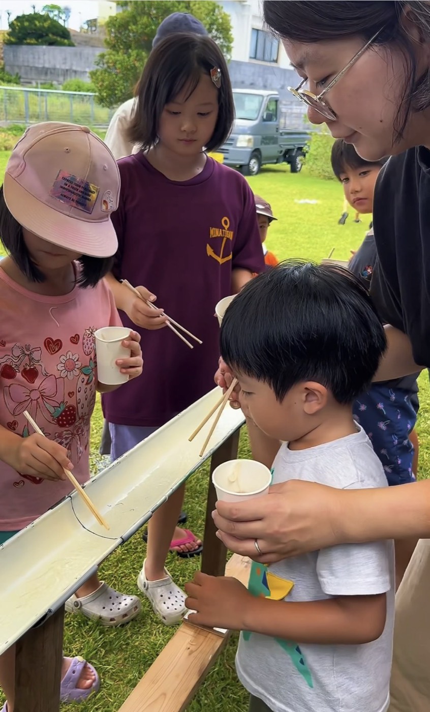 小さな子どもがそうめんをすくうのを大人がそばで見守る様子