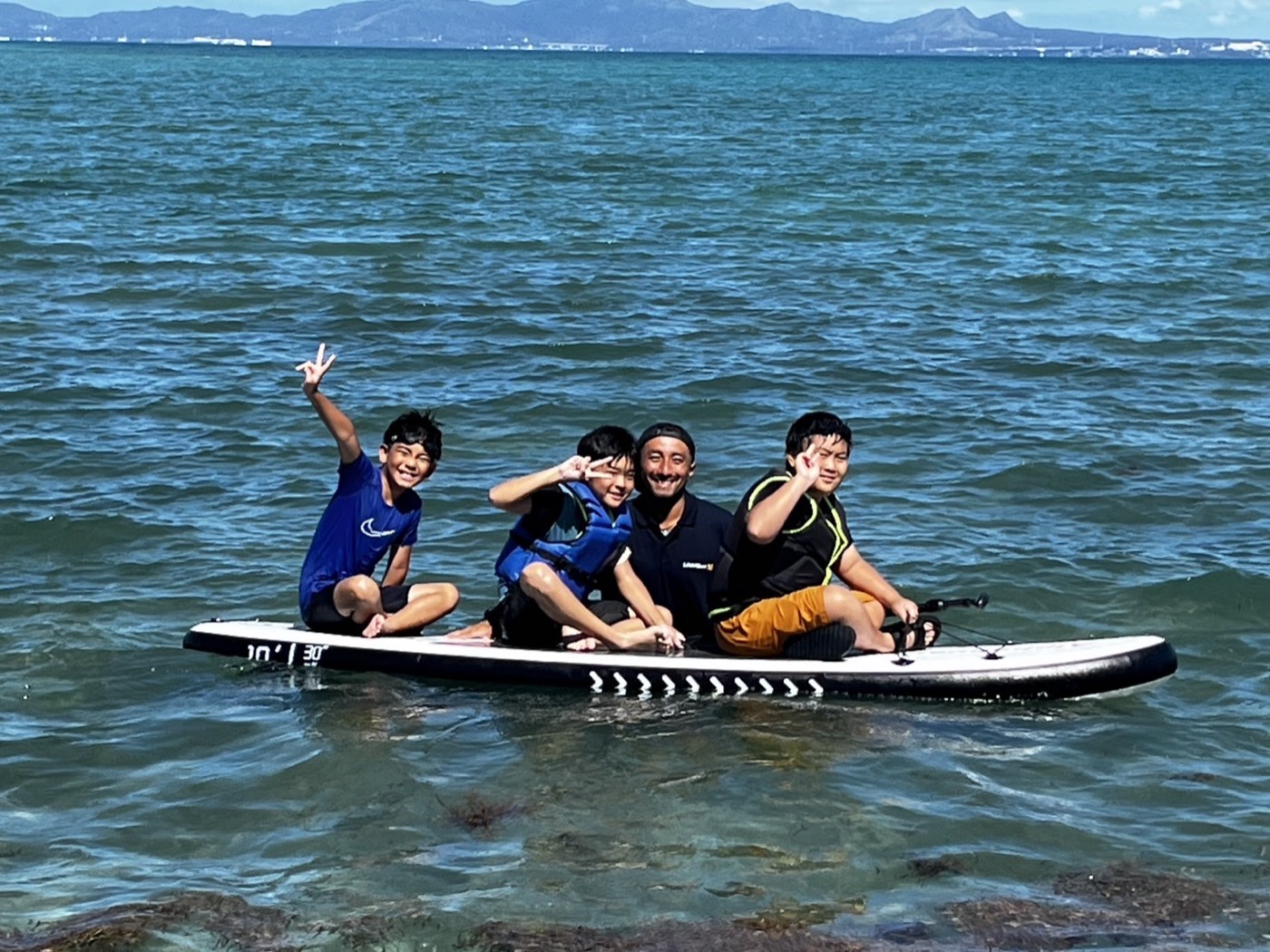 SUPボードの上でピースをする3人の子どもとスタッフ
