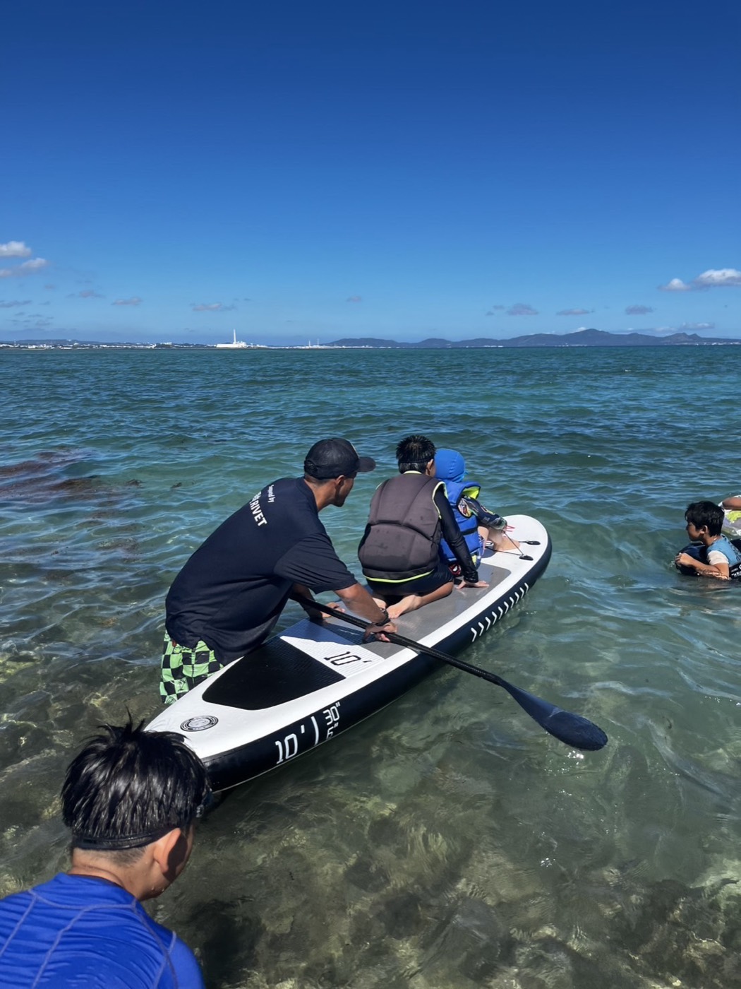 浅瀬でSUPボードに乗った子どもを後ろから支えて押し出すサポーター